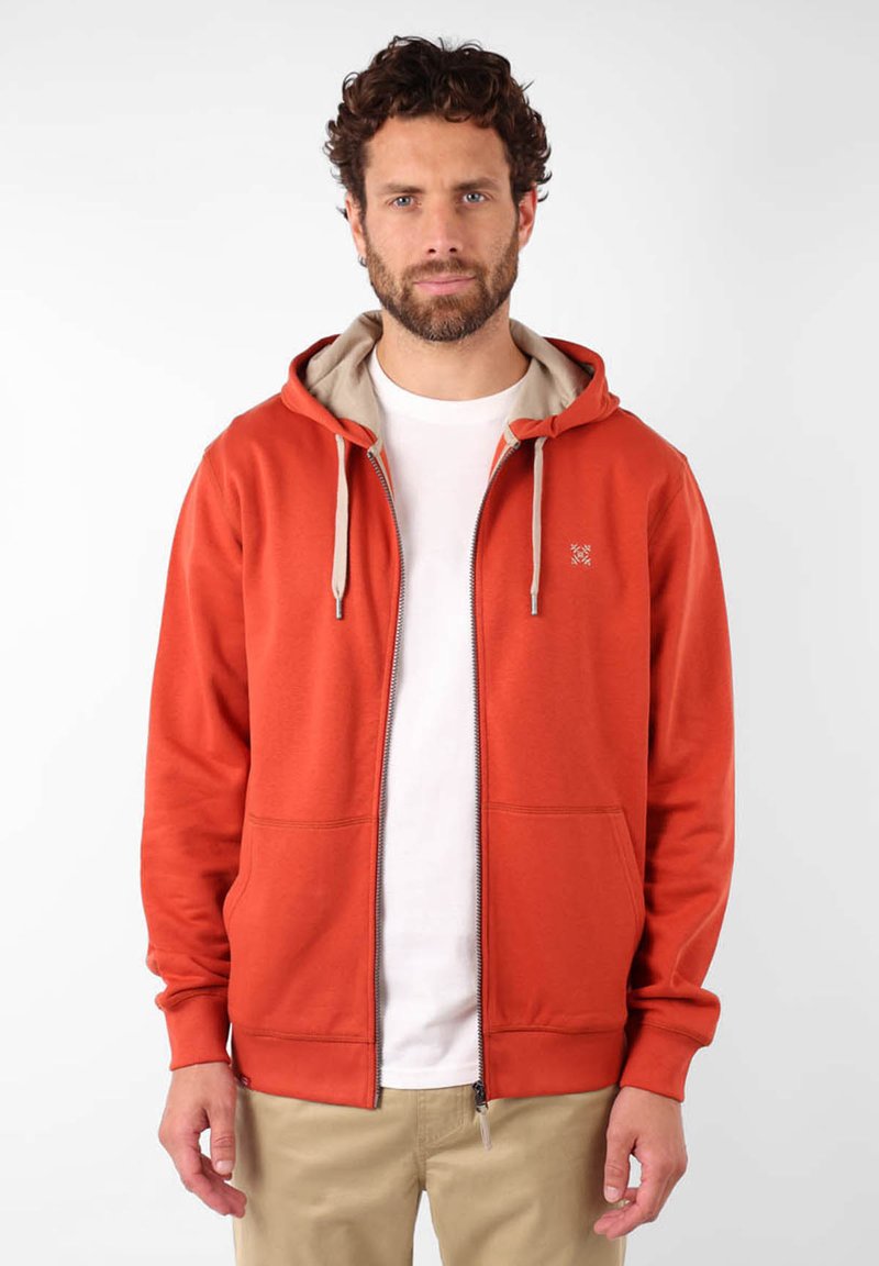 Grosse veste à capuche zippée rouge avec doublure beige, cordon de serrage et poches avant. Fabriquée en tissu doux, elle présente un logo sur la poitrine.