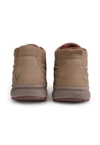 Braune Wildleder-Stiefeletten mit runden Schäften, minimaler Naht und strukturierten Außensohlen. Mit einem kleinen Hühnerlogo auf der Rückseite.