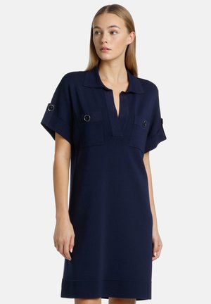 Donkerblauw korte mouwen jurk met een kraaghals, twee borstzakken en ronde hardwareaccenten op de mouwen. Zachte textuur, relaxte pasvorm.