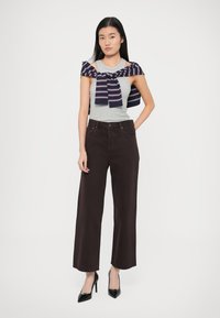 Šedé tílko s námořnicky modrým a krémově pruhovaným svetrem uvázaným přes ramena, v kombinaci s vysoce střiženými tmavě hnědými širokými kalhotami a černými podpatky.