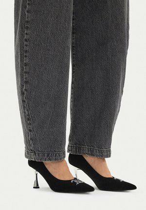 Scarpe nere con punta a punta e tacco medio con tacchi argentati indossate con jeans grigio scuro a gamba dritta.