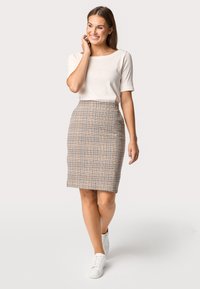 Een getailleerde beige geruite kokerrok met blauwe en bruine lijnen, gecombineerd met een crèmekleurige top met korte mouwen en witte sneakers.