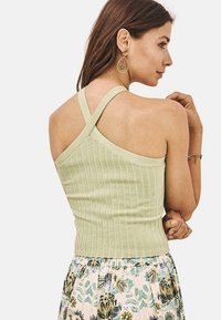 Top corto de canalé verde claro con un diseño ajustado y tirantes cruzados en la espalda, combinado con una falda de estampado floral.