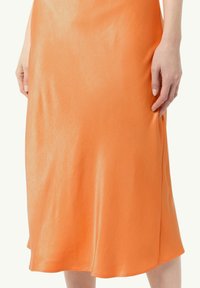 Pomarańczowa satynowa spódnica midi o gładkiej, błyszczącej fakturze. Posiada płynącą sylwetkę oraz subtelne boczne rozcięcie. Długość dołu spódnicy kończy się tuż poniżej kolana.