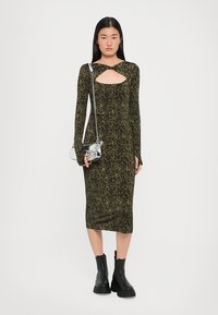 Long-sleeve, fitted dress in dark green with leopard print, featuring a keyhole cutout. Paired with a silver mini handbag and black boots.