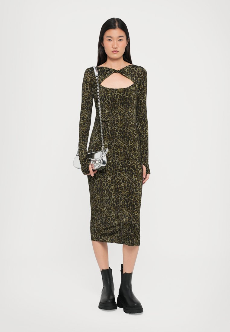 Robe ajustée à manches longues de couleur vert foncé avec motif léopard, présentant une découpe en cœur. Assortie à un mini sac à main argenté et des bottes noires.