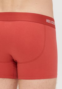 Boxer briefs vermelhos elásticos com uma textura suave, apresentando uma cintura elástica com a marca. O design inclui costuras curvadas para melhorar o ajuste.