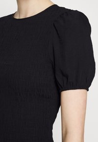 Blusa preta com um design texturizado e pregueado, com mangas curtas bufantes e um decote redondo. O tecido parece leve e suave.