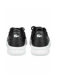 Sneakers in pelle nera con suole in gomma bianca, dotate di lacci neri e di un logo Lacoste bianco sul tallone. Finitura liscia, forma arrotondata.