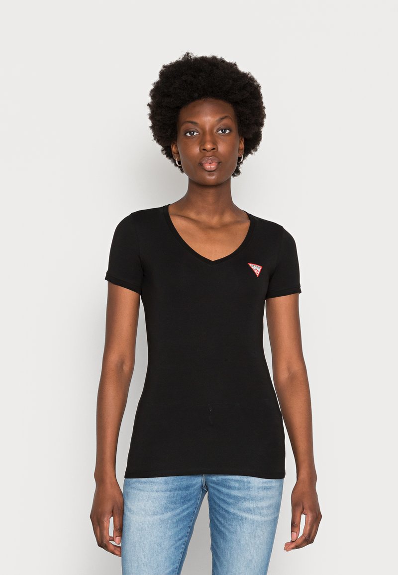 T-shirt nera a maniche corte con scollatura a V e design aderente. Presenta un piccolo logo triangolare rosso sul petto sinistro. Abbinato a jeans azzurri chiari.