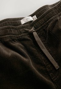 Dark brown corduroy pants with elastic waistband, drawstring tie, and visible white brand label reading "NEXT Relaxed Tapered Fit."