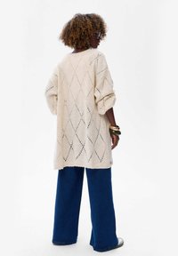 Crème-kleurige gebreide trui met een ruitpatroon, oversized pasvorm en geribbelde zoom. Gepaard met wijde blauwe jeans.