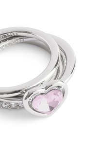 Silver ring set featuring three interlocking bands, one with a heart-shaped pink gemstone and small clear accent stones. Smooth, polished finish.
