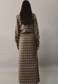 Ensemble chemise à manches longues et jupe à carreaux marron. Le matériau semble doux avec une texture lisse. Comprend des détails de boutons aux poignets et une silhouette cintrée.