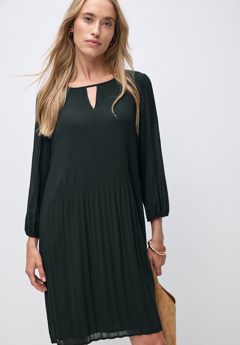 Dunkelgrünes, plissiertes Kleid mit einem Schlüsselloch-Ausschnitt, langen elastischen Ärmeln und einer fließenden Silhouette. Glatte Textur und knielanger Schnitt.