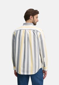 Camisa de rayas en tela gris, amarilla y blanca. Presenta un cuello abotonado, mangas largas y una canesú con pliegues en la parte posterior.