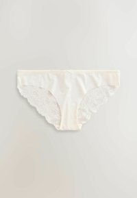 Kreemo krāsā apakšveļa bikini ar mežģīņu apdari, kas ietver gludu audumu priekšpusi un viļņotu mežģīņu akcentus sānos, izceļot ziedu rakstu.