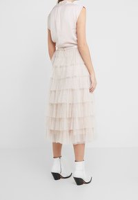 Jupe en tulle rose clair à étages avec des paillettes, design en couches, taille cintrée, associée à un top sans manches ajusté et des bottines blanches à la cheville.