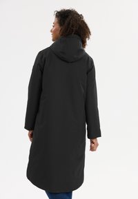 Manteau long imperméable noir avec capuche, présentant un tissu texturé et une coupe droite. La longueur atteint le mollet, adapté aux temps froids.