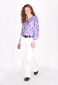 Paarse bomberjack met bloemenprint, voorzien van een ritssluiting aan de voorkant en geribbelde manchetten, gecombineerd met witte wijde broekspijpen en zwarte schoenen.