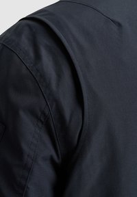 Tela de un azul marino oscuro con una textura suave, que presenta una costura de hombro ajustada y un diseño limpio y minimalista. Sin patrones ni acentos visibles.