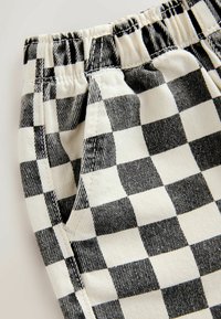 Primer plano de pantalones de tela a cuadros en blanco y negro con cintura elástica y detalles de costuras en los bolsillos laterales.