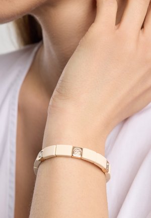 Cremefarbener Armband aus rechteckigen Gliedern, mit metallischen Akzenten und kleinen quadratischen Verzierungen auf ausgewählten Gliedern.