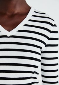 Haut à manches longues en V noir et blanc à rayures, fabriqué dans un tissu doux, présentant des rayures horizontales uniformément réparties avec un léger élasticité.