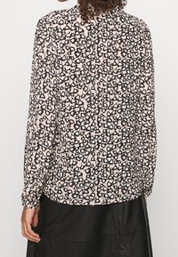 Langarmbluse in hellem Pink mit einem schwarzen und blauen Leopardenmuster. Aus weichem Stoff mit runder Halslinie und gerafften Ärmeln.
