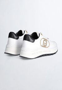 Sneakers bianchi in pelle con accenti neri, suola bianca sollevata, dettagli del logo dorato e testo "CREATI PER FARSI SENTIRE FANTASTICO" sul lato.