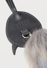 Μπρελόκ από μαύρο πατινέ δέρμα με ανάγλυφο λογότυπο "DIESEL", διαθέτει ασημί κρίκο και προσκολλημένη τεχνητή γούνα σε γκρι αποχρώσεις.