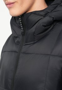 Μαύρο μπουφάν τύπου πούφτερ με φερμουάρ στο μπροστινό μέρος, κουκούλα και καλυμμένη υφή. Το υλικό φαίνεται γυαλιστερό με απλές γραμμές και διακριτή ραφή αντίθεσης.