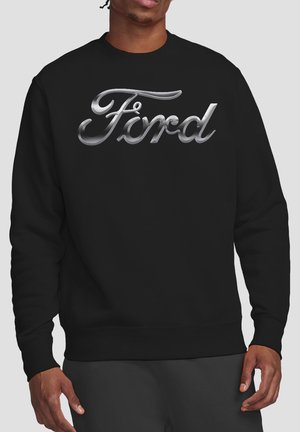 Person wearing a black sweatshirt with a large silver metallic "Ford" logo across the chest on a plain background.