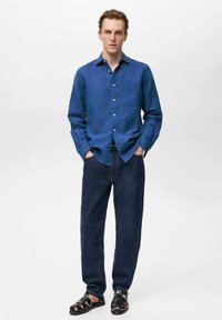 Blauwe linnen shirt met lange mouwen en knoopsluiting, gecombineerd met donkere denim jeans en zwarte strappy sandalen. Eenvoudig ontwerp, relaxte pasvorm.