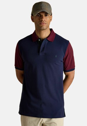 Kurzarm-Polohemd in Marineblau mit weinroten Schultern, ausgestattet mit einer Knopfleiste mit zwei Knöpfen, weicher Textur und einem Logo auf der Brust.