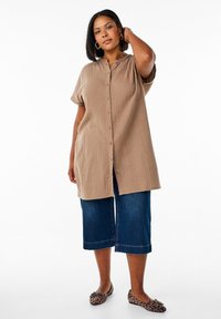 Tan button-up shirt with short sleeves and a relaxed fit, paired with cropped dark blue denim pants and animal print flats.