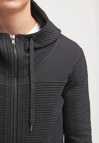 Černá mikina se zipem, ribbovanou strukturou, vysokým límcem a šňůrkami, s hladkým zipem a přiléhavým střihem.