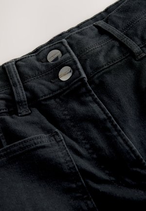 Schwarze Jeanshose mit flachem Bund, zwei metallischen Knöpfen, sichtbaren Nähten und strukturierter Stoffqualität sowie Seitentaschen.