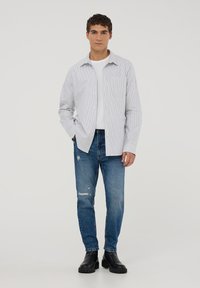 Camicia a righe blu chiaro e bianca, indossata sopra una maglietta bianca. Abbinata a jeans strappati blu e stivali neri alla caviglia.