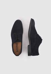 Chaussures en daim bleu marine avec une texture lisse, présentant un design à lacets et une semelle plate en caoutchouc. Une chaussure est ornée d'accents en œillets.