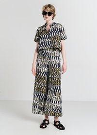 Set composto da camicia corta e pantaloni a gamba larga con audaci motivi in nero, bianco e verde oliva. Tessuto leggero con una trama liscia e maniche corte.