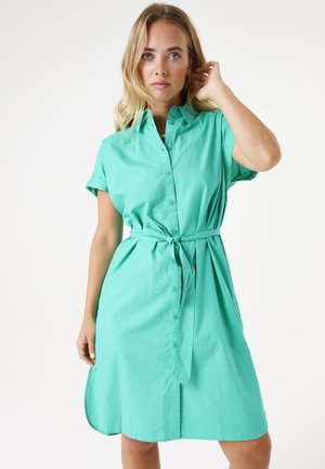 Robe chemise turquoise en tissu léger, avec une fermeture à boutons, des manches courtes, une ceinture à la taille et un ourlet incurvé.