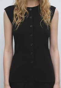 Black sleeveless top featuring a ribbed texture, a buttoned front closure, and a slight slit at the hem for added detail.