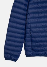 Giacca imbottita blu navy con design a trapunta, polsini elasticizzati e dettaglio della tasca laterale con zip. Materiale liscio e leggero.