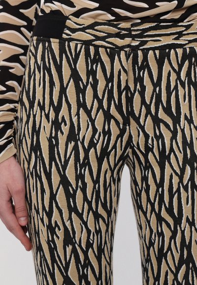 Trousers with a textured, stretchy fabric featuring a black and beige abstract pattern. Elastic waistband. Close-up view of the design.