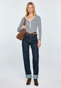 Gestreiftes Langarmshirt mit Knopfleiste, dunkle Denim-Hosen in hoher Taille mit Umschlägen und einer braunen Wildleder-Handtasche. Braune Knöchelschuhe.