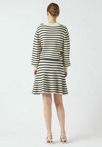 Raidalline neulemekko pitkillä hihoilla; musta ja kerma väliin vaihdellen; kellottava hame tiukalla vyötäröllä; malli pukeutuneena vaaleisiin korkokenkiin.