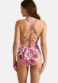 Maillot de bain une pièce floral rouge et blanc avec un dos nu, des bretelles croisées et un lien à nouer à la taille. Tissu lisse et extensible.