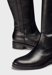 Bottes noires en cuir jusqu'au genou avec une texture lisse, bout arrondi, petit talon empilé et coutures discrètes sur les côtés.