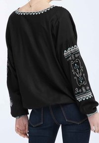 Blusa nera con maniche lunghe e puffate. Presenta un intricato ricamo turchese lungo le maniche e il decolleté. Tessuto morbido con una vestibilità ampia.